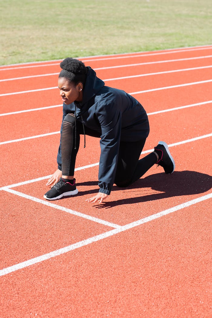 African American woman runner preparing to start a race on an outdoor track in bright daylight.